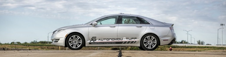 Side view of silver vehicle with AutonomouStuff logo